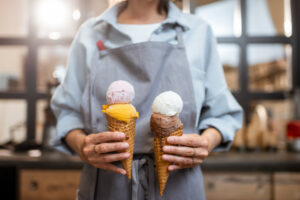 Female,Seller,Holding,Two,Yummy,Ice,Creams,In,Waffle,Cone