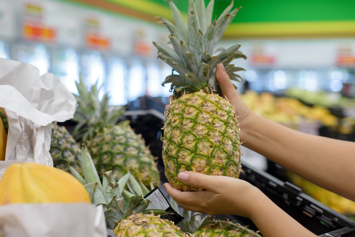 Female,Hands,Picking,Up,A,Pineapple,From,A,Supermarket,Shelf.
