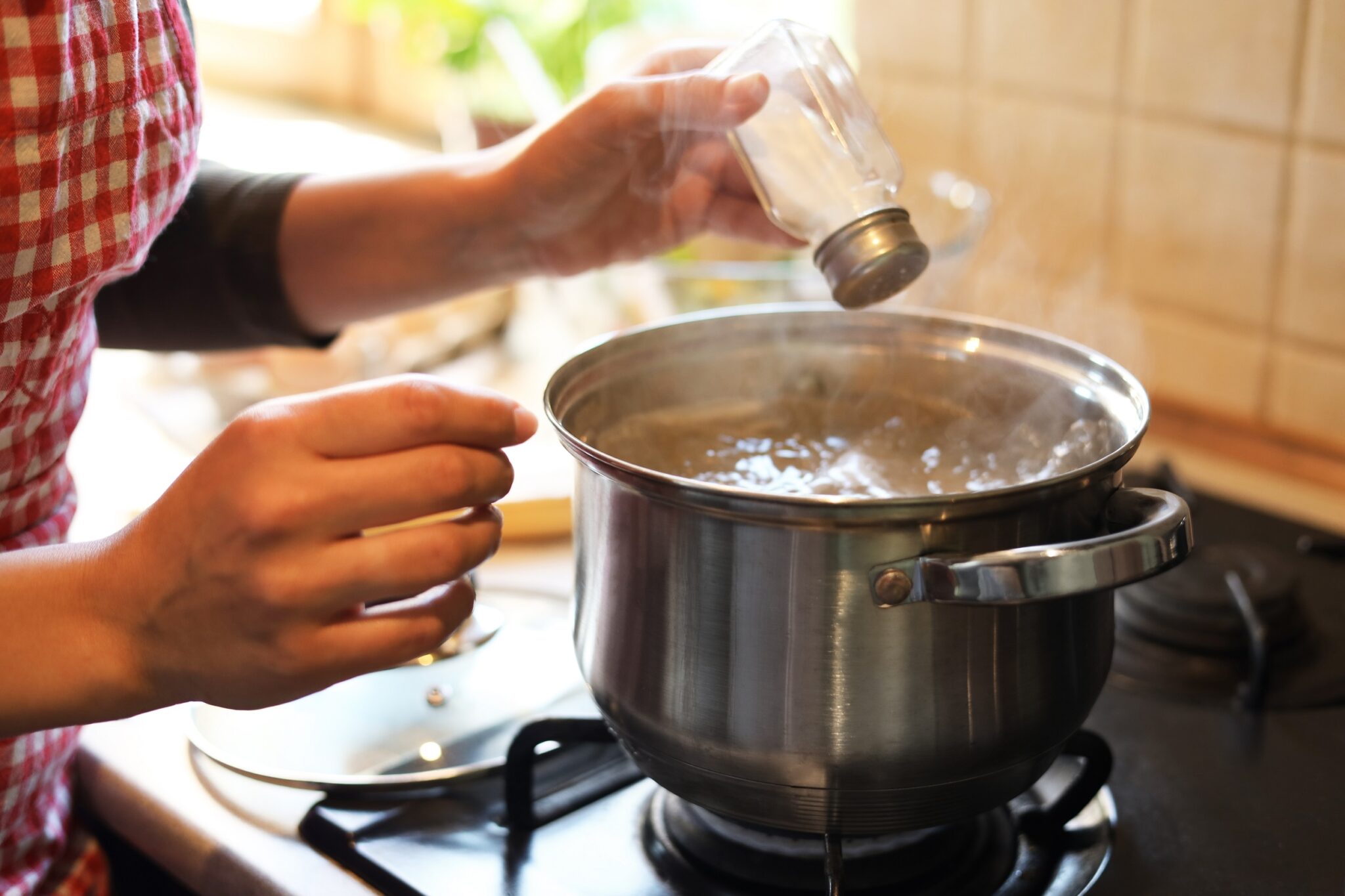 Woman,Adding,Salt,To,Boiling,Water,In,Pot,On,Stove