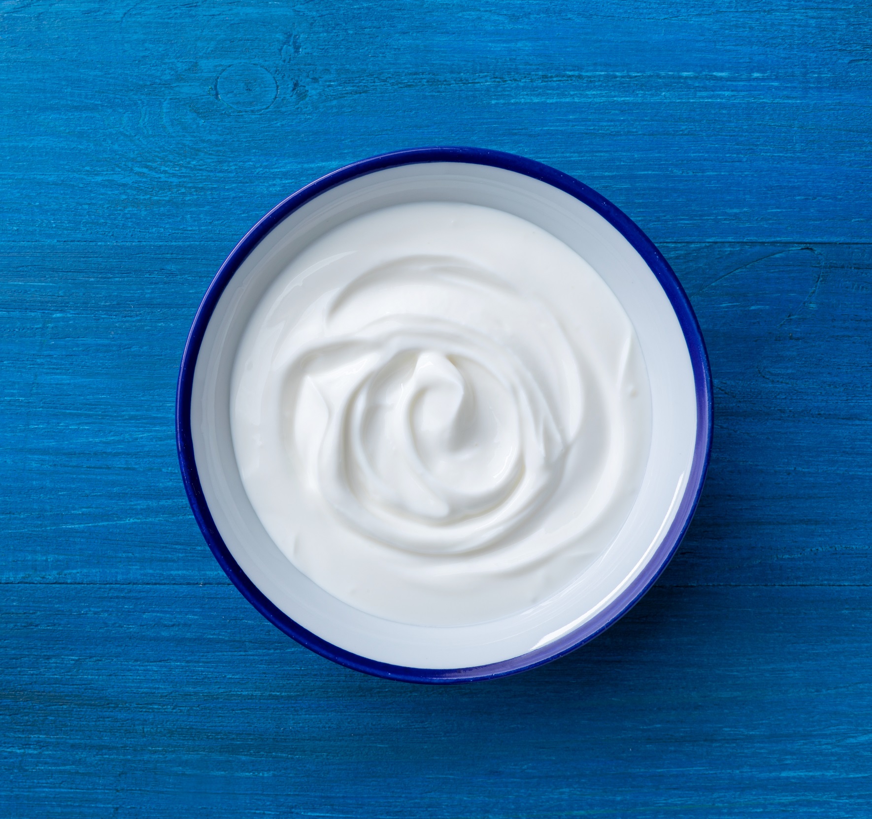 Greek,Yogurt,In,Bowl,On,Blue,Wooden,Table,Top,View.