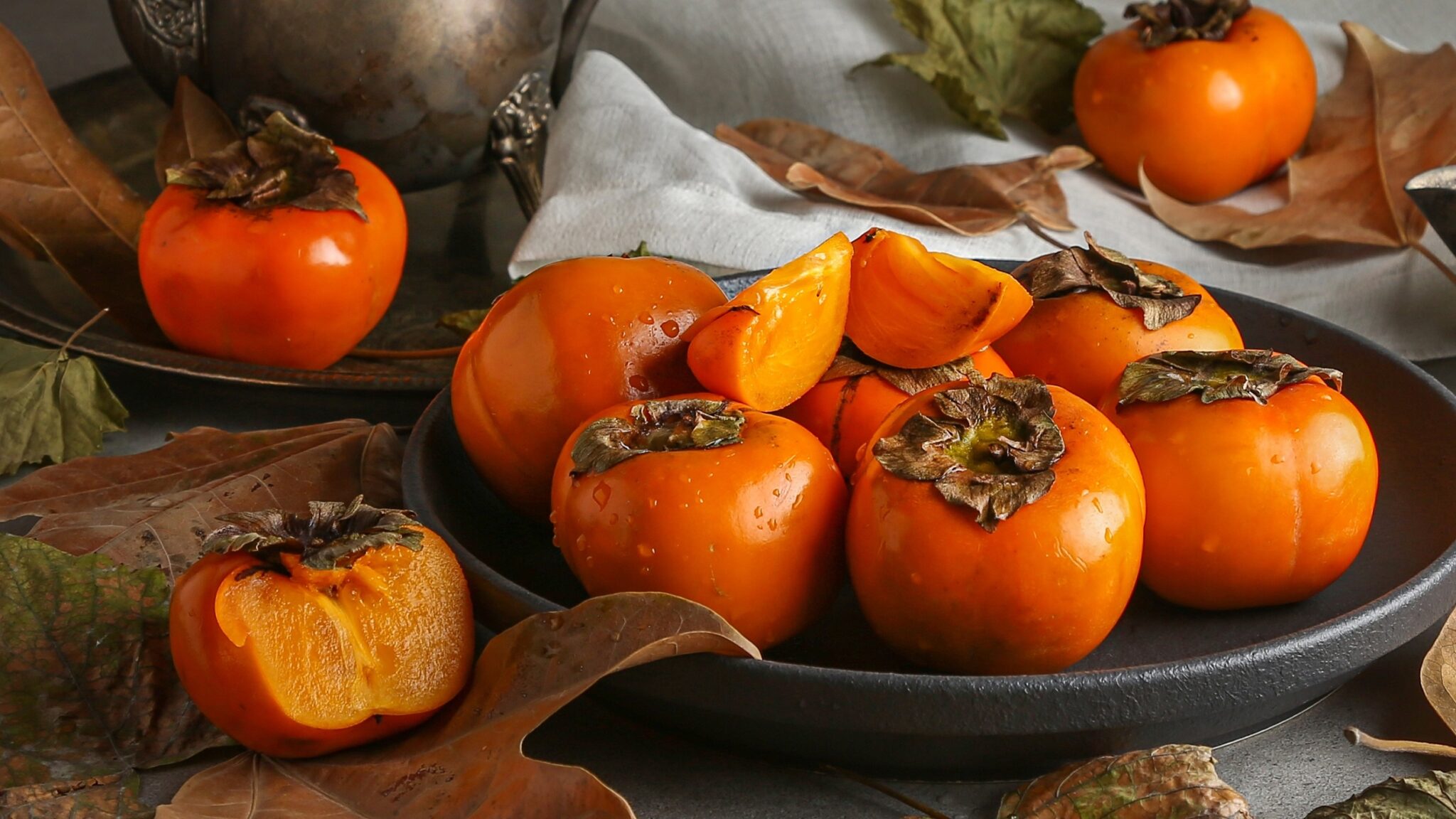 Several,Ripe,Persimmons,And,Persimmon,Pieces,On,Big,Black,Plate