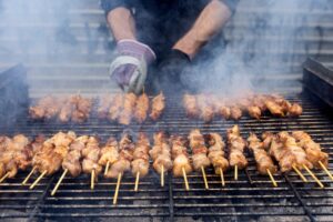 A,Grill,Filled,With,Skewers,Of,Meat,Cooking,Over,Open