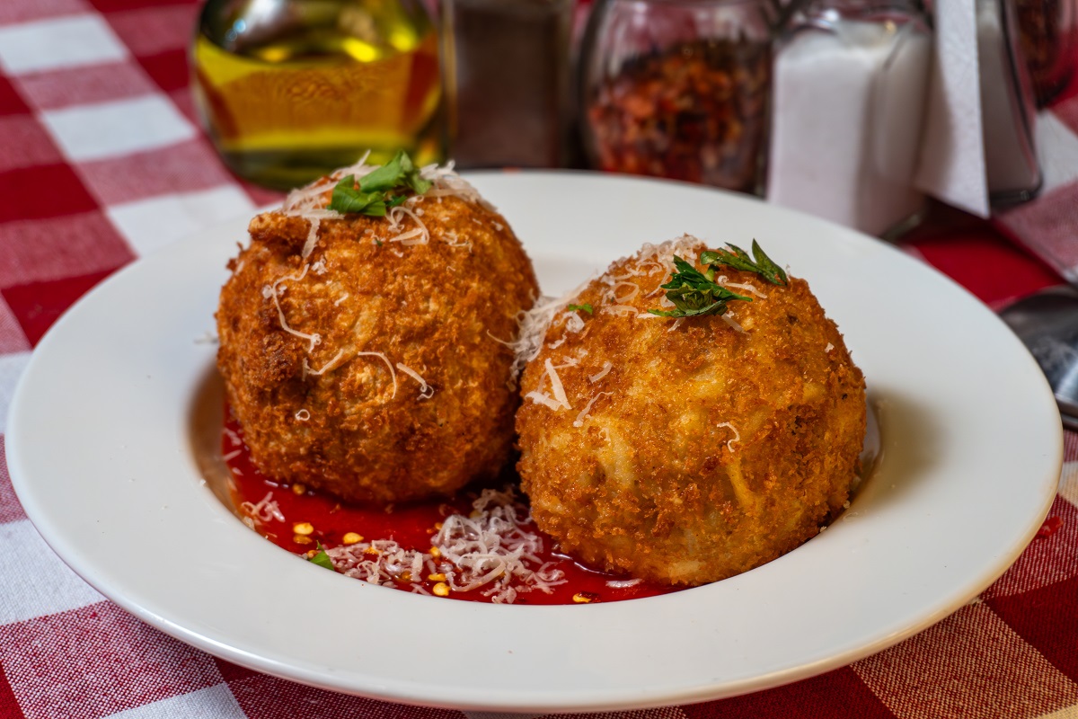 Two,Golden,Crispy,Arancini,Topped,With,Grated,Cheese,And,Herbs,