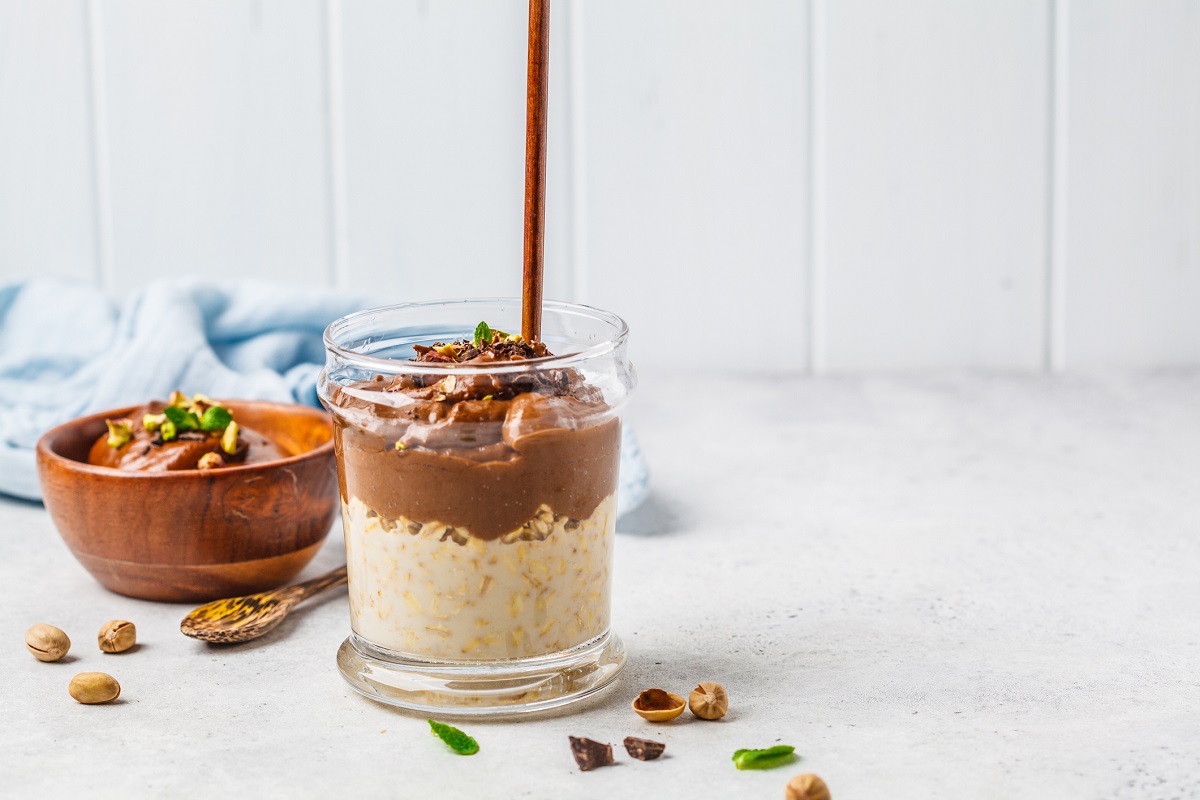 Overnight oatmeal with milk and chocolate mousse in glass on a white background.